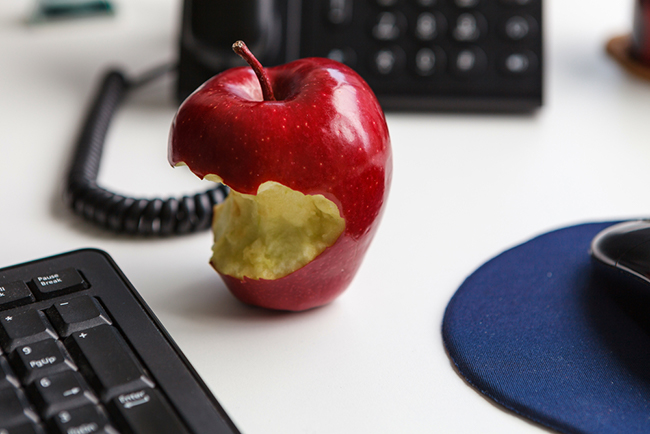 A half eaten apple sitting on a desk next to a keyboard and a telephone.