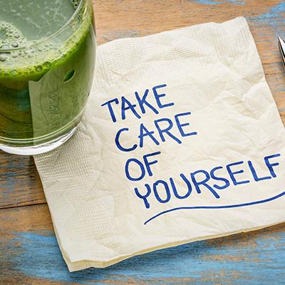 Take care of yourself written in blue ink on a napkin next to a glass of green juice