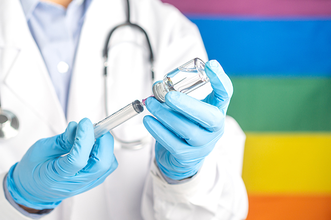 Person in lab coat and gloves uses syringe in front of Pride flag background