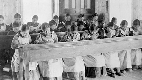 Native American children sitting at a desk in a Residential School.