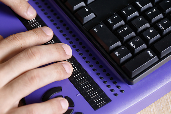 Fingers touching braille on computer keyboard
