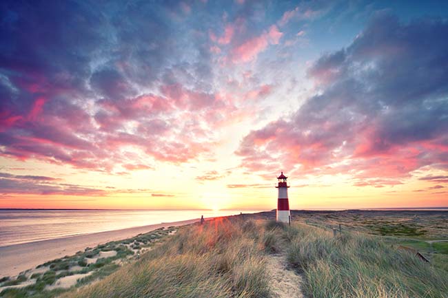 A red and white lighthouse next to the ocean at sunrise 