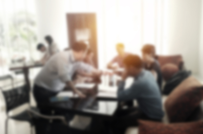 A deliberately out of focus image of people sitting at a table having a meeting.