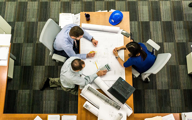 Overhead shot of 3 people sitting at a table collaborating on a project.