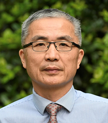 Chinese American Branch Chief Dr. Yuling Hong wearing a grey suit jacket, light blue shirt, and lavender tie in front of a grey background.