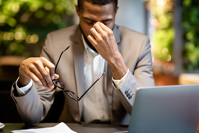 Exhausted black male sitting at computer desk feels fatigue, burnout, and stress.