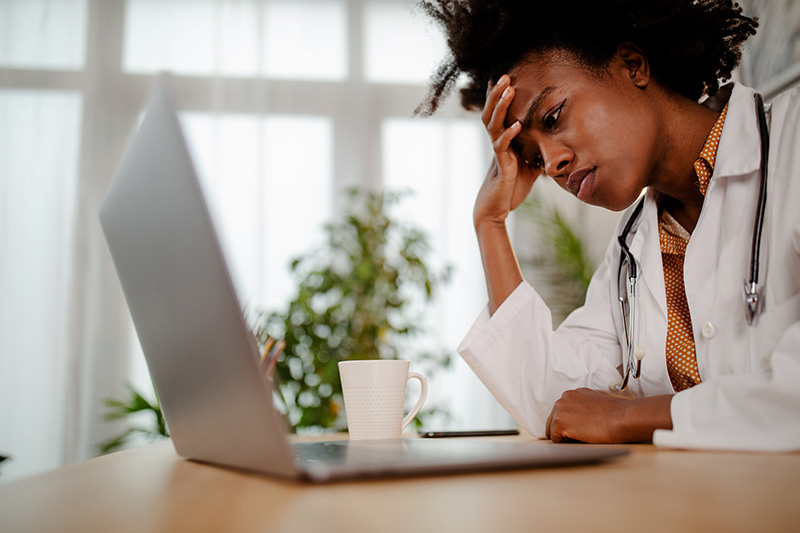 Image of a stressed African American medical professional, upset, exhausted, feeling frustrated, depressed, tired, and holding head in forehead.