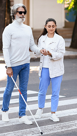 A young woman helps a blind man cross the street in the crosswalk area