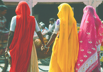 Three East Indian women walking down the street holding hands.