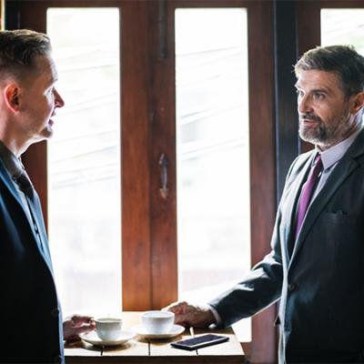 Two men, in business attire, having a conversation over coffee.