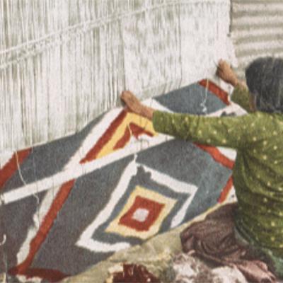 Women weaves traditional Navajo blanket hanging on a wall.