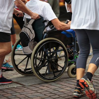 A group of people jogging. One of the runners is pushing a man in a wheelchair.