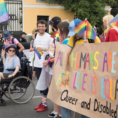 Group of people at PRIDE parade holding up banner that says: All Humans Are Equal; All Love is Equal: Queer and Disabled