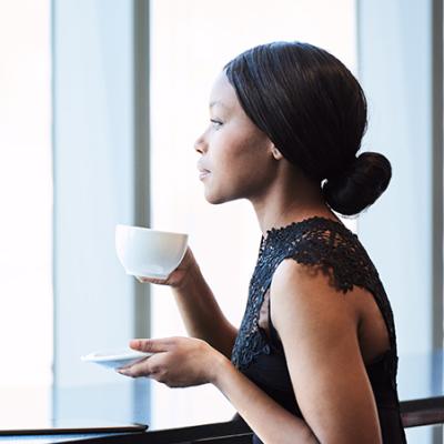 A Black woman holding a cup of coffee while staring out of the window