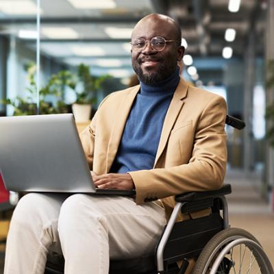 Smiling African American man in a wheelchair holding a laptop. 
